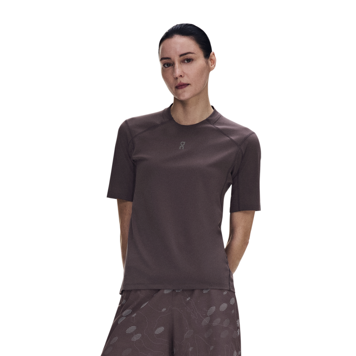 A woman modeling a short-sleeve athletic top in a dark brownish-gray color, paired with matching patterned shorts, against a solid white background. - On Trail-T Solar (Women's) - Mulberry