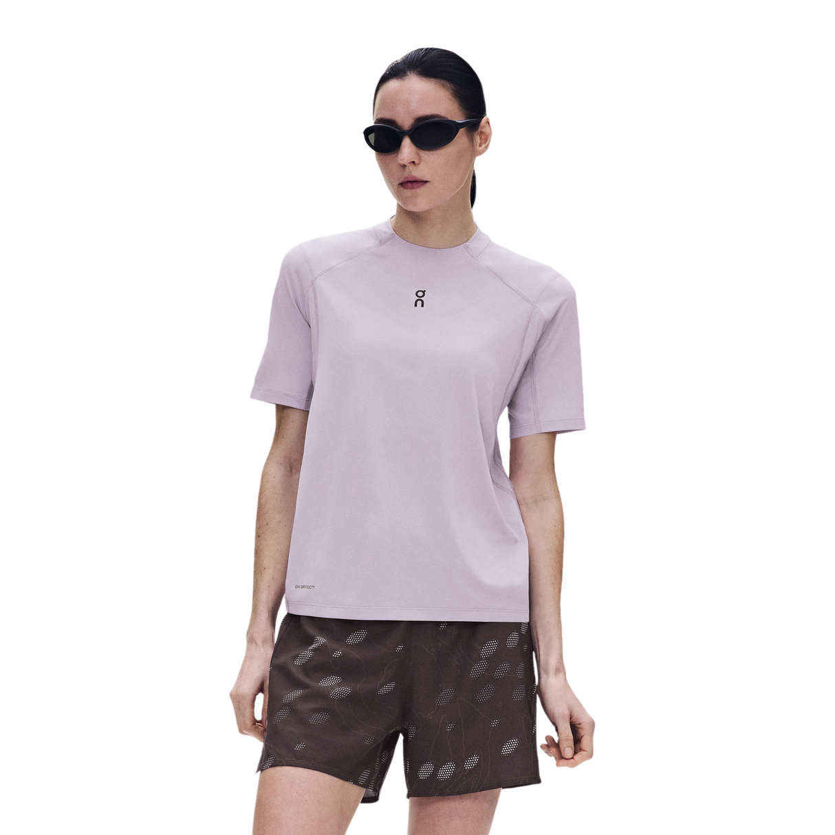 A woman modeling a light purple short-sleeve athletic t-shirt with a small black logo on the chest, paired with dark patterned shorts, against a solid white background. - On Trail-T Solar (Women's) - Foxglove