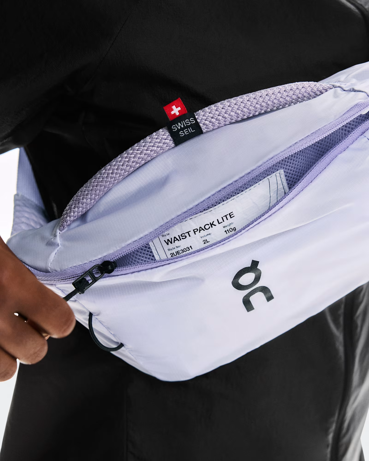 White waist pack with visible branding held by a person against a black background - On Waist Pack 2L Lite - Thistle