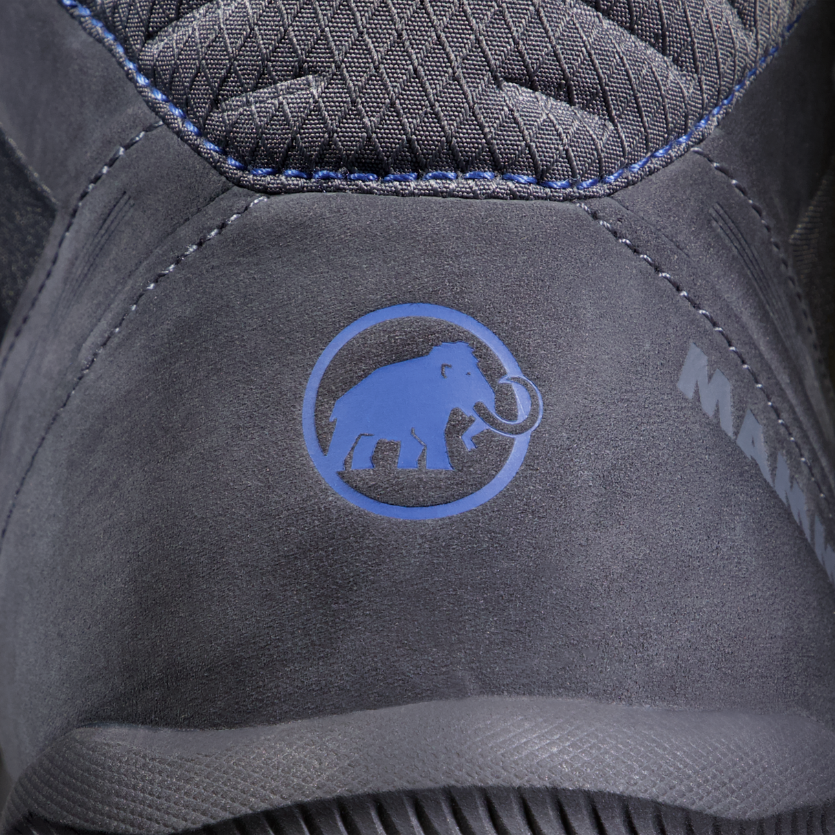 Close-up of a dark gray suede shoe with a blue Mammut logo on the heel, showing textured stitching and the brand name partially visible. - Mammut Mercury IV Mid GORE-TEX (Men's) - Dark Titanium/Black