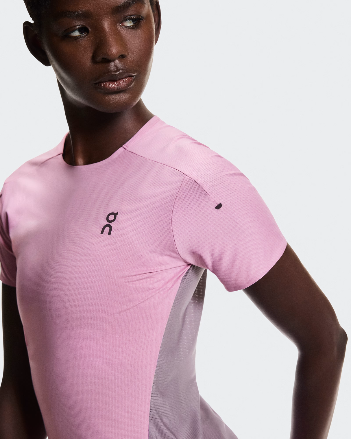 Person wearing a pink athletic shirt with a brand logo on a light gray - On Performance-T (Women's) - Dewberry/Sakurabackground