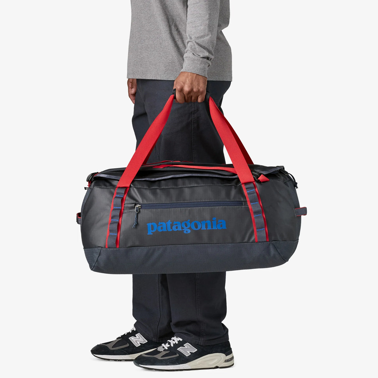 Person holding a Patagonia duffel bag with red straps on a white background - Patagonia Black Hole Duffel 55L - Smolder Blue w/Amanita Red