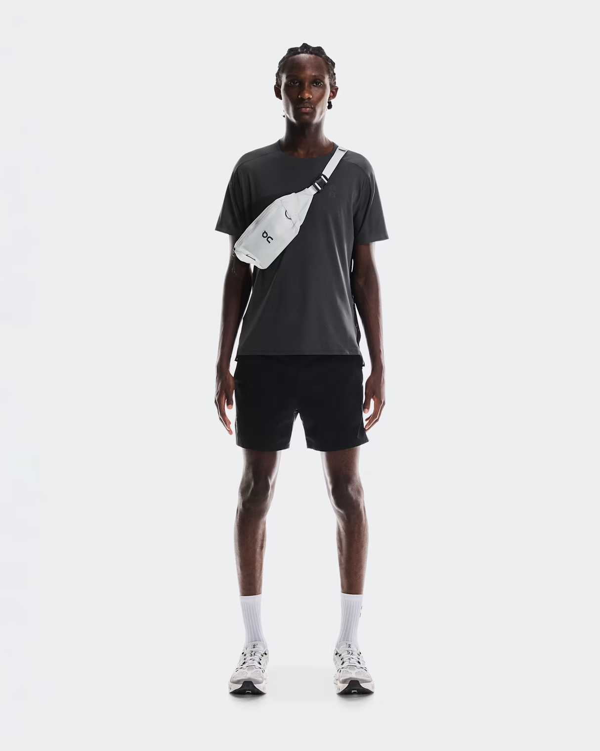 Person wearing a dark t-shirt, black shorts, white socks, and black shoes with a crossbody bag on a white background - On Waist Pack 2L Lite - Glacier