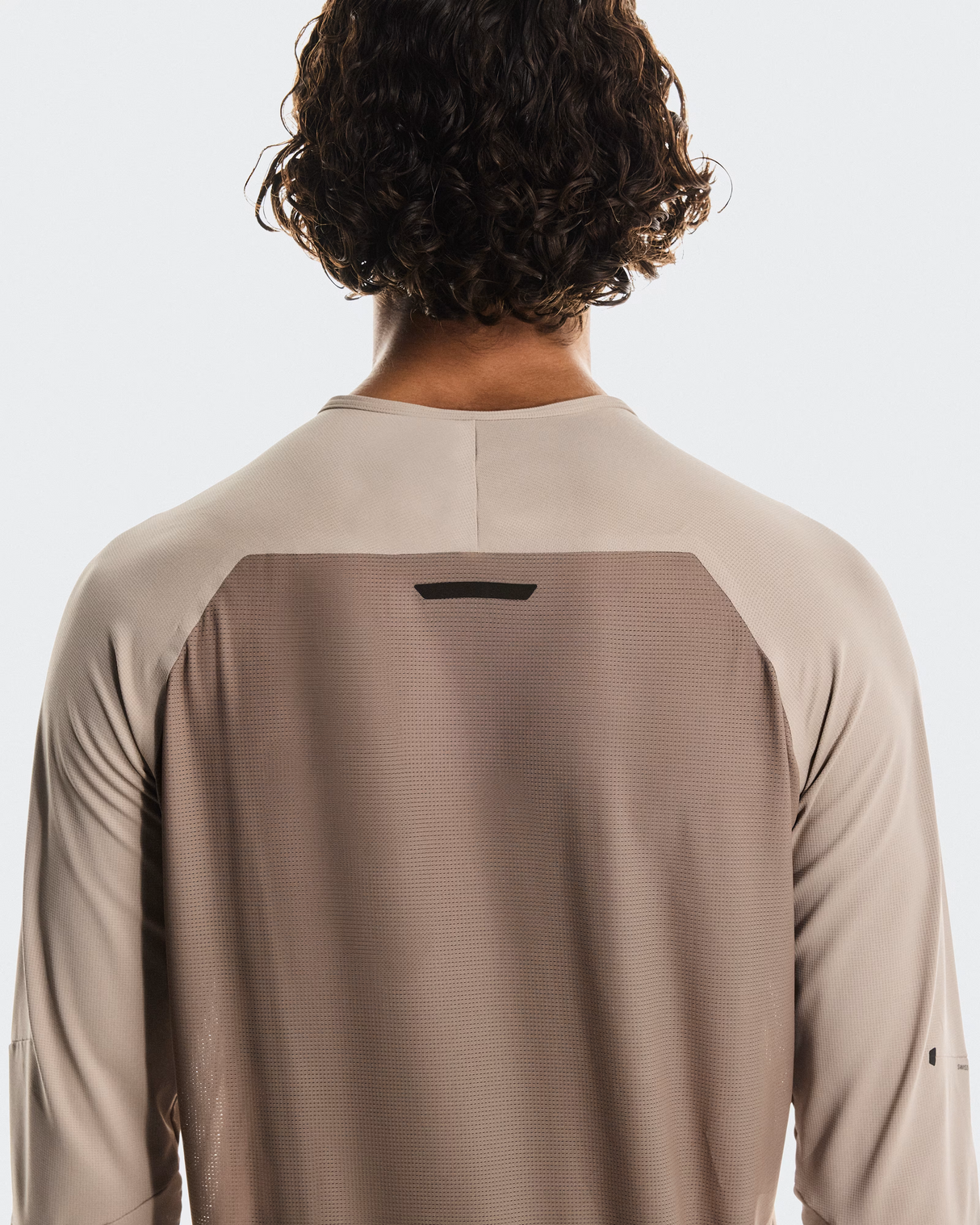 Person wearing a beige long-sleeve shirt with a small black logo on the back against a white background - On Performance Long-T (Men's) - Desert/Cinder