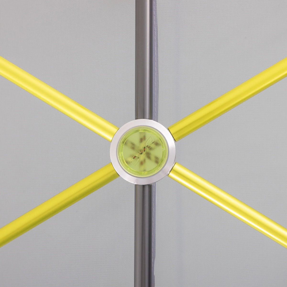 Close-up of a chair or stool crossbar assembly with four bright yellow tubular bars radiating from a central silver metal hub, with a light green circular insert in the middle, set against a light gray background. - Sea to Summit Sentinel Tent
