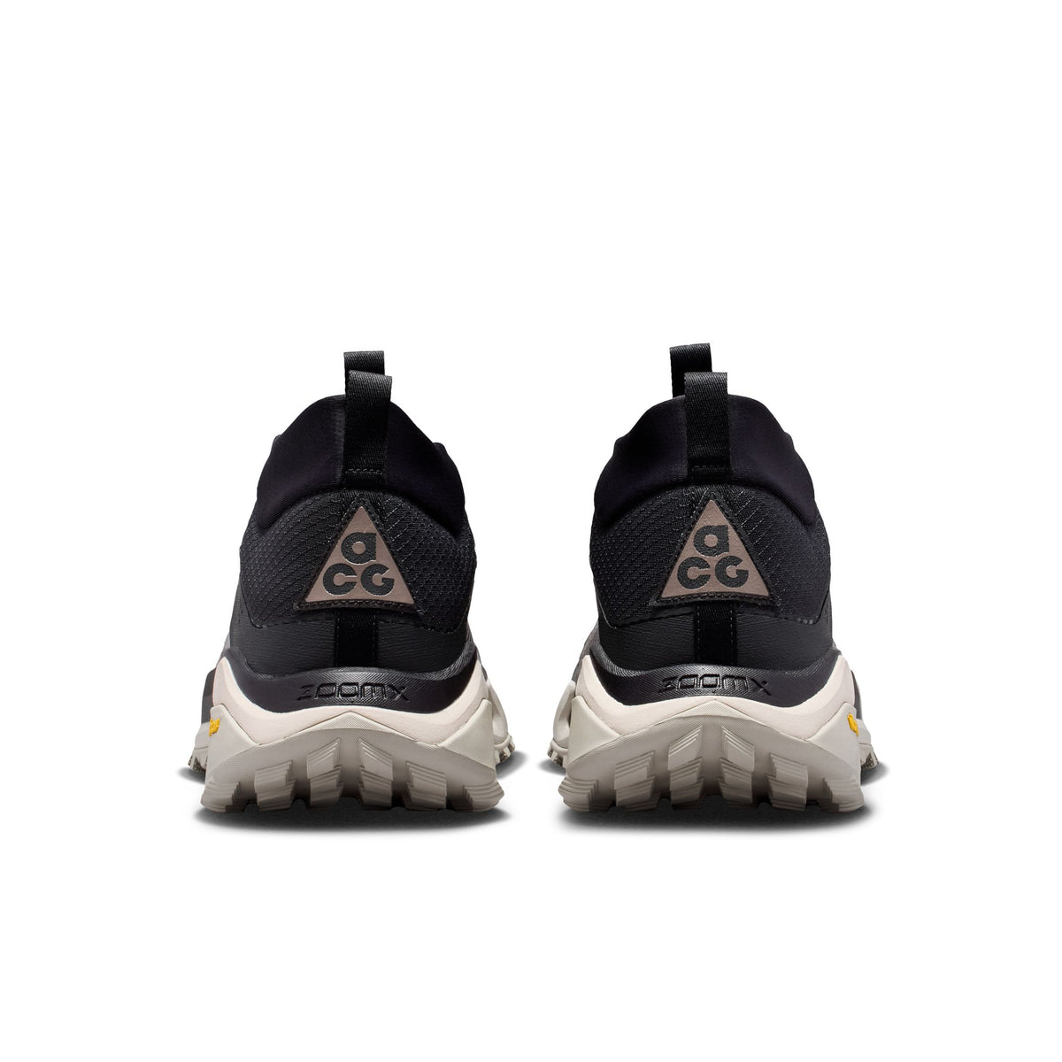 A pair of black and dark gray trail running shoes shown from the rear, featuring a black mesh upper, a gray triangular ACG logo on the heel, and a chunky off-white sole with 'ZOOMX' branding. - Nike ACG Zegama Hike Shoes (Men's) - Black/Ironstone-Cream II