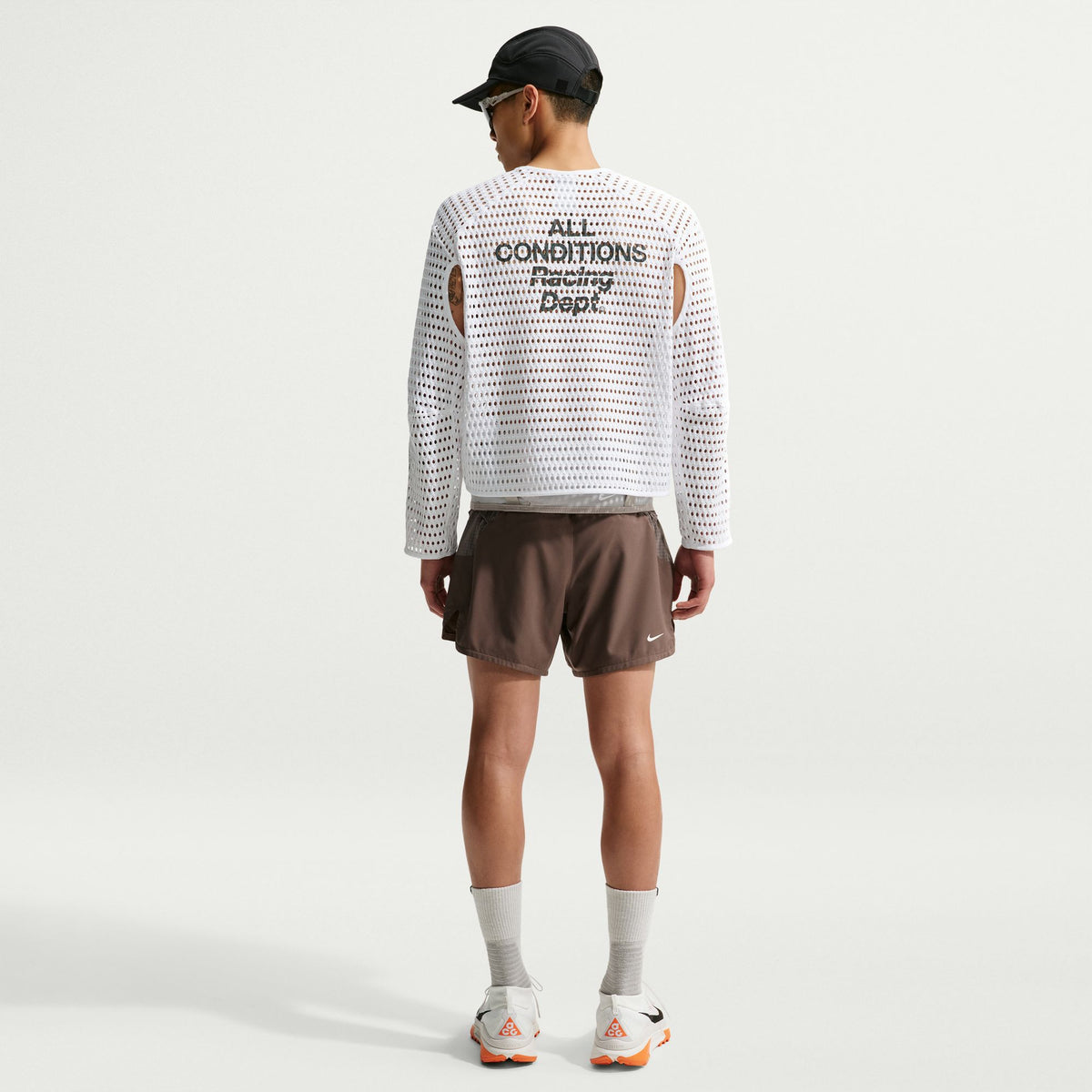Person wearing a white long-sleeve shirt with text and brown shorts on a light gray background - Nike ACG Radical Airflow NXT Dri-FIT Long-Sleeve Trail-Running Top (Men's) - White/Anthracite