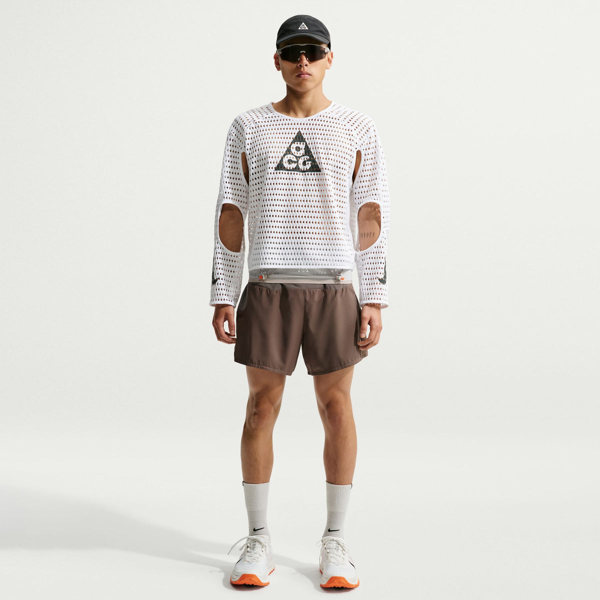 Person wearing a white long-sleeve shirt with cut-out design and brown shorts on a white background - Nike ACG Radical Airflow NXT Dri-FIT Long-Sleeve Trail-Running Top (Men's) - White/Anthracite