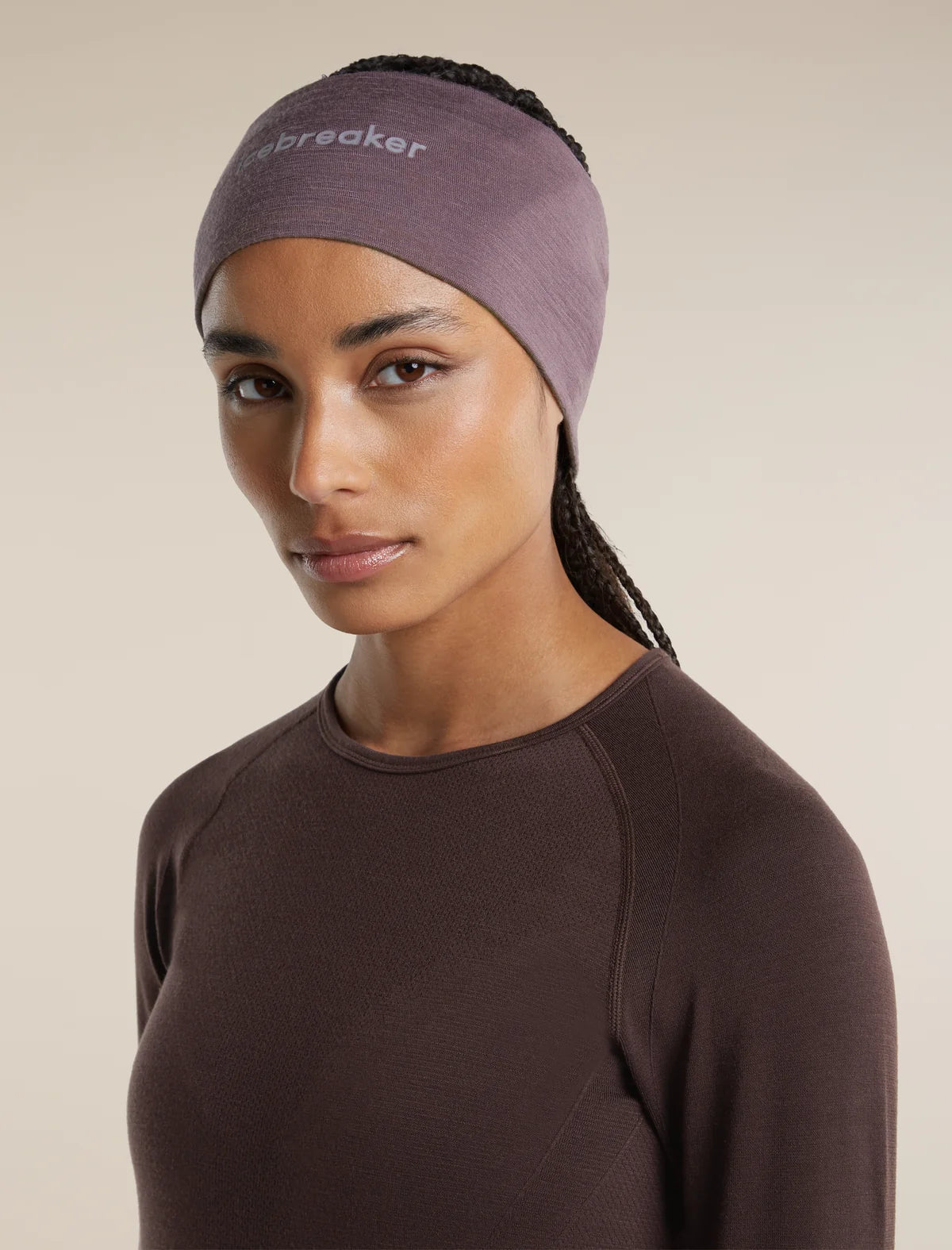 A woman wearing a dusty mauve athletic headband with the brand name 'breaker' printed in white on the forehead, paired with a dark brown long-sleeve top, against a solid beige background. - Icebreaker Merino 200 Oasis Headband (Unisex) - Grey Plum