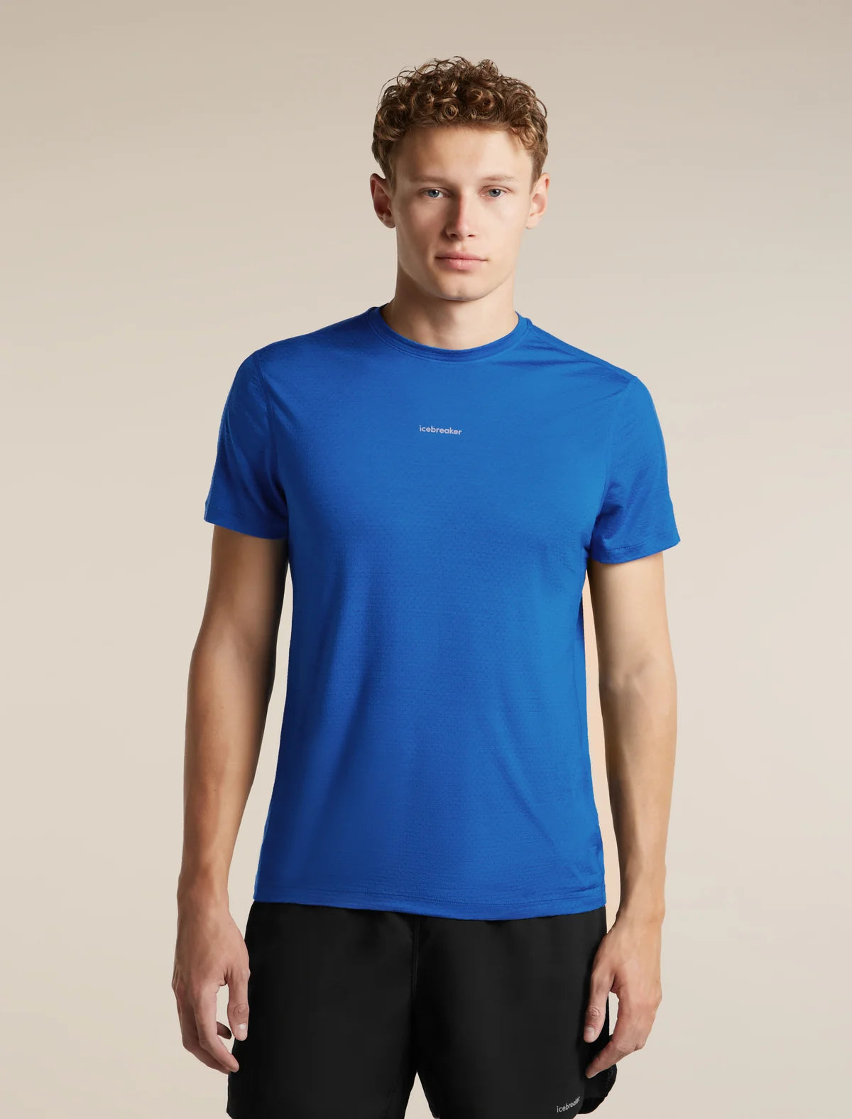 A man wearing a bright blue short-sleeve athletic t-shirt with a small white logo on the chest, paired with black shorts, against a solid beige background. - Icebreaker Merino Blend 125 Cool-Lite Speed Short Sleeve T-Shirt (Men's) - Lazurite