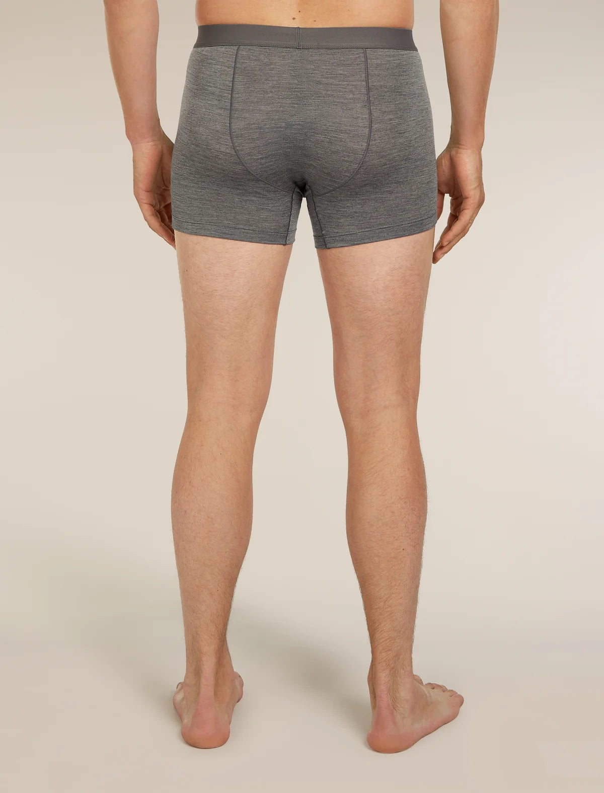 A man viewed from the back wearing heather gray boxer briefs, standing barefoot against a plain light beige studio background. - Icebreaker Merino Blend 125 Cool-Lite Anatomica Boxers (Men's) - Gritstone Heather