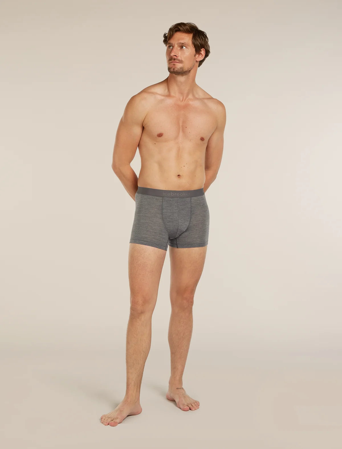 A shirtless male model stands barefoot against a plain light beige studio background, wearing gray heathered boxer briefs. - Icebreaker Merino Blend 125 Cool-Lite Anatomica Boxers (Men's) - Gritstone Heather
