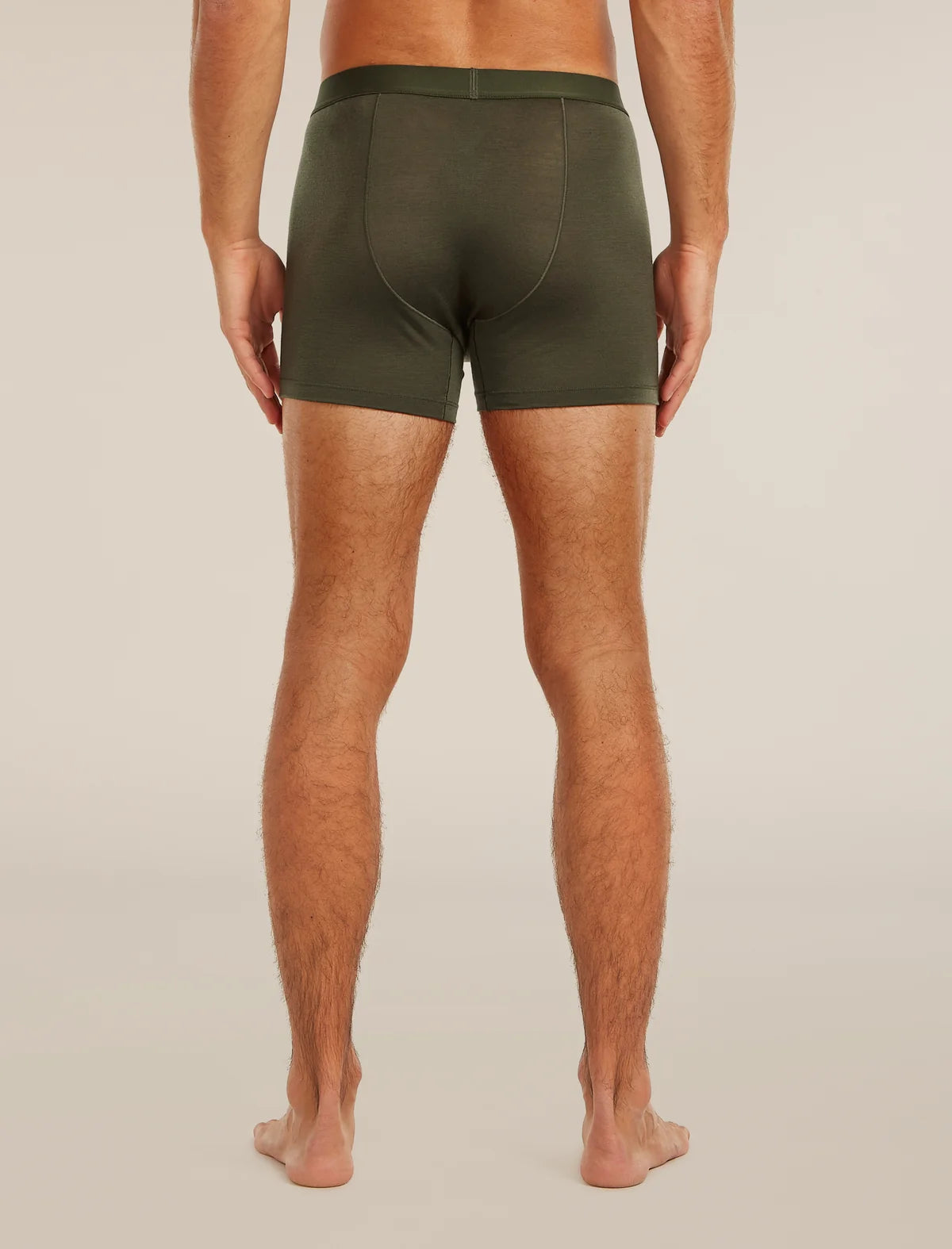 A man viewed from the back wearing olive green boxer briefs, standing barefoot against a plain light beige studio background. - Icebreaker Merino Blend 125 Cool-Lite Anatomica Boxers (Men's) - Dark Loden
