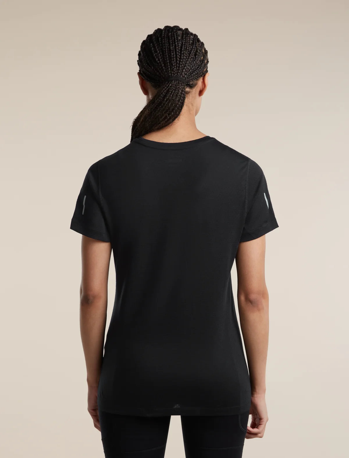 Rear view of a woman wearing a black short-sleeve athletic T-shirt with subtle reflective details on the sleeves, set against a solid beige background. - Icebreaker Merino Blend 125 Cool-Lite Speed Short Sleeve T-Shirt (Women's) - Black