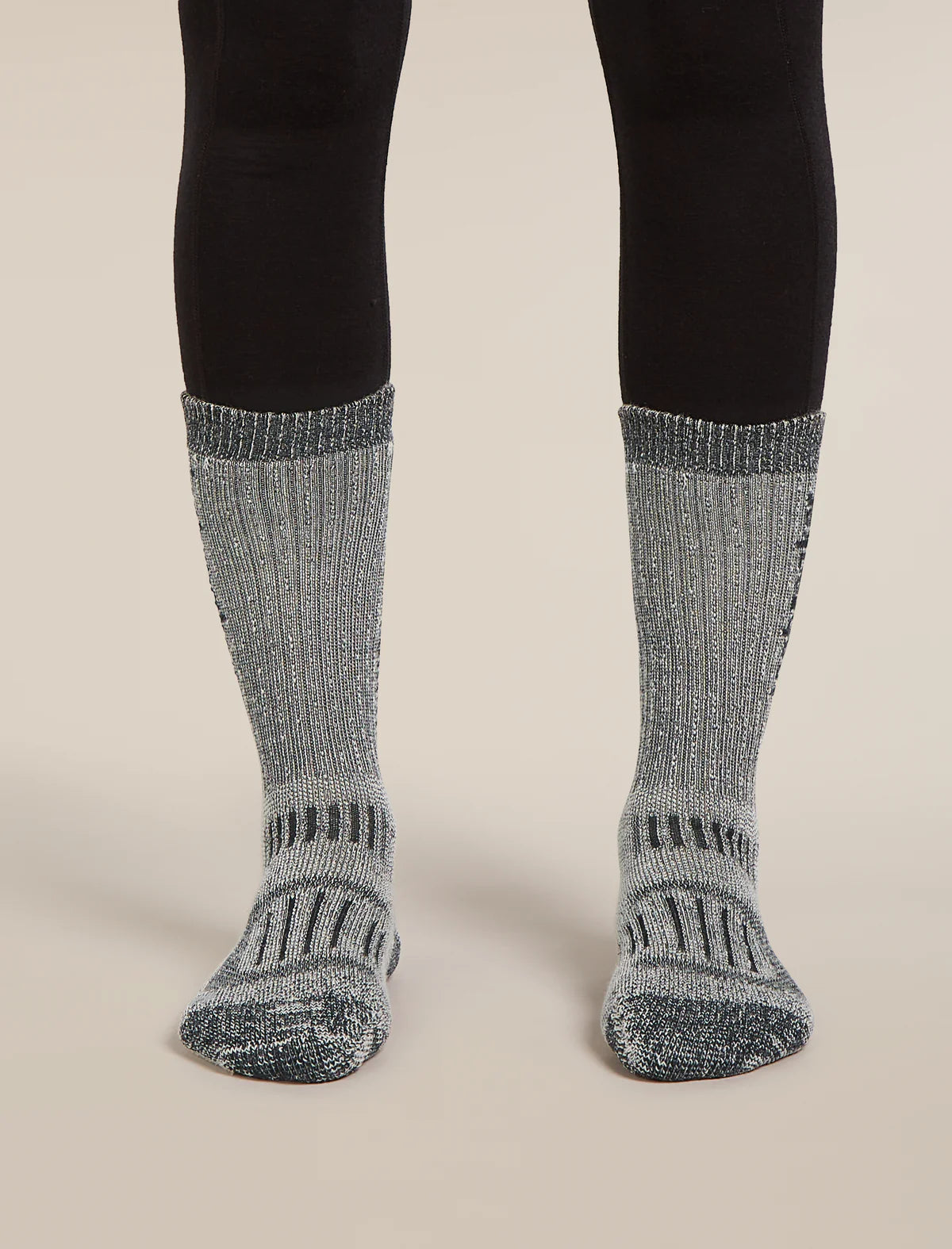 Gray socks with black patterns worn with black leggings on a beige background - Icebreaker Merino Hike+ Mountaineer Mid Calf Socks (Women's) - Jet Heather/Black