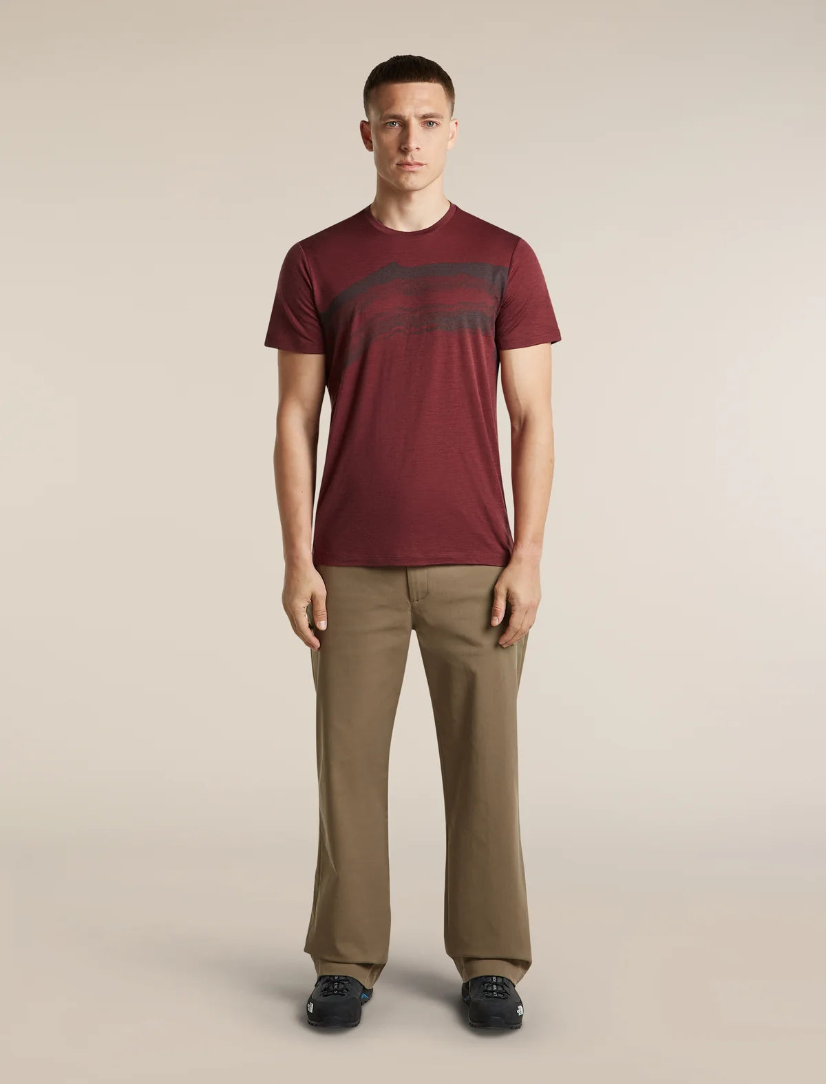 A man modeling a short-sleeve crewneck t-shirt in maroon with a dark graphic print across the chest, paired with khaki trousers and dark loafers, against a solid light beige background. - Icebreaker Merino 150 Tech Lite Short Sleeve T-Shirt Getaway (Men's) - Port