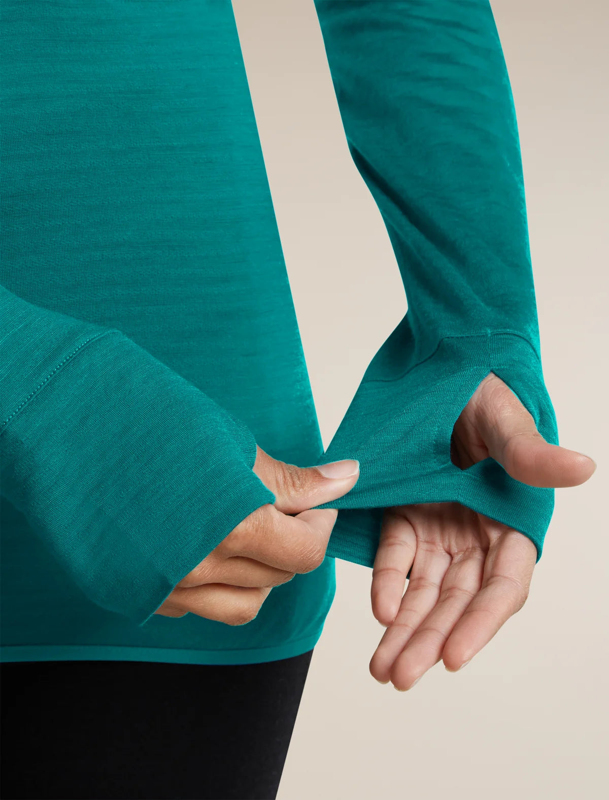 A close-up of a person wearing a teal long-sleeve athletic top with thumbholes, pulling the sleeve slightly to show the stretch and fit of the fabric. - Icebreaker Merino Blend 200 RealFleece Descender Long Sleeve Half Zip (Women's) - Tidal Teal