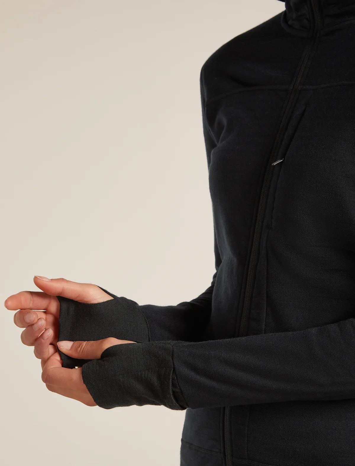 Close-up of a person wearing a black long-sleeve athletic zip jacket, showing the cuffs and torso against a plain light beige studio background. - Icebreaker Merino Blend 300 RealFleece Descender Long Sleeve Zip Hoodie (Women's) - Black