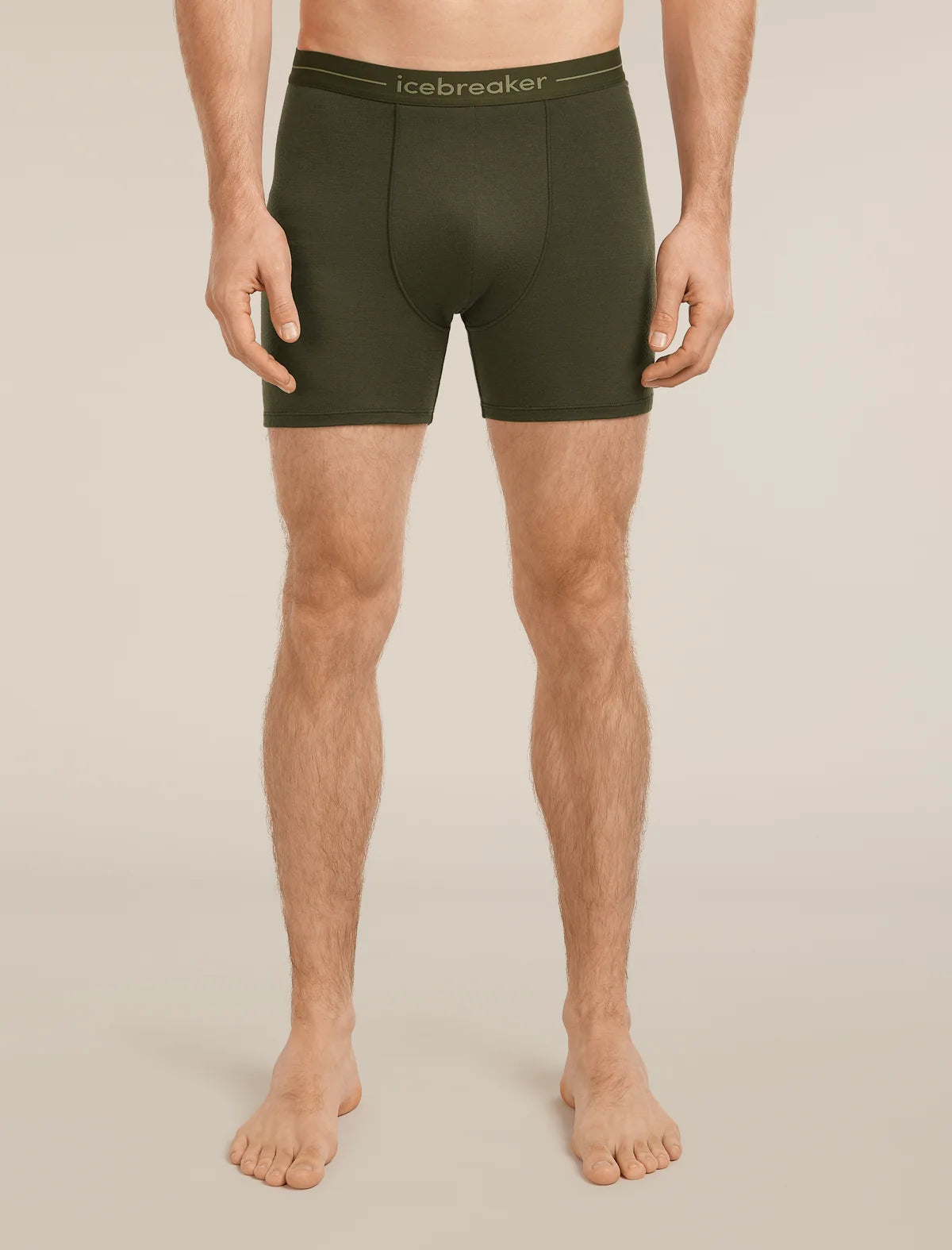 A man modeling dark olive green men's boxer briefs with a matching elastic waistband featuring the 'icebreaker' brand name, shown against a solid light beige background. - Icebreaker Merino 150 Anatomica Boxers (Men's) - Dark Loden