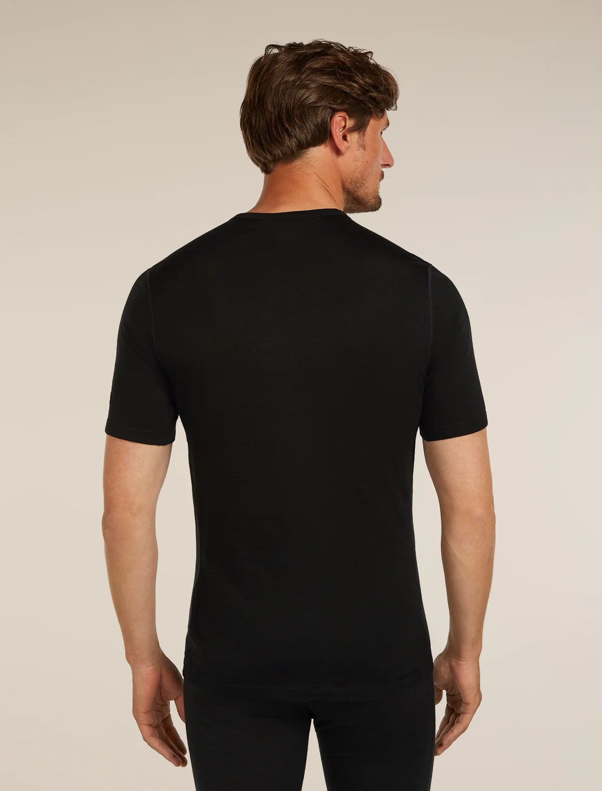 A man viewed from the back wearing a black short-sleeve crew-neck t-shirt and black pants, set against a plain beige studio background. - Icebreaker Merino 200 Oasis Short Sleeve Crew Neck (Men's) - Black