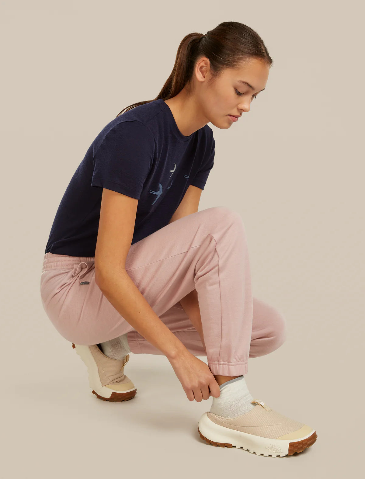 Woman wearing a navy t-shirt and pink pants, tying her beige sneakers on a neutral background - Icebreaker Merino Multisport Light Mini Socks (Women's) - Ecru Heather/Alloy