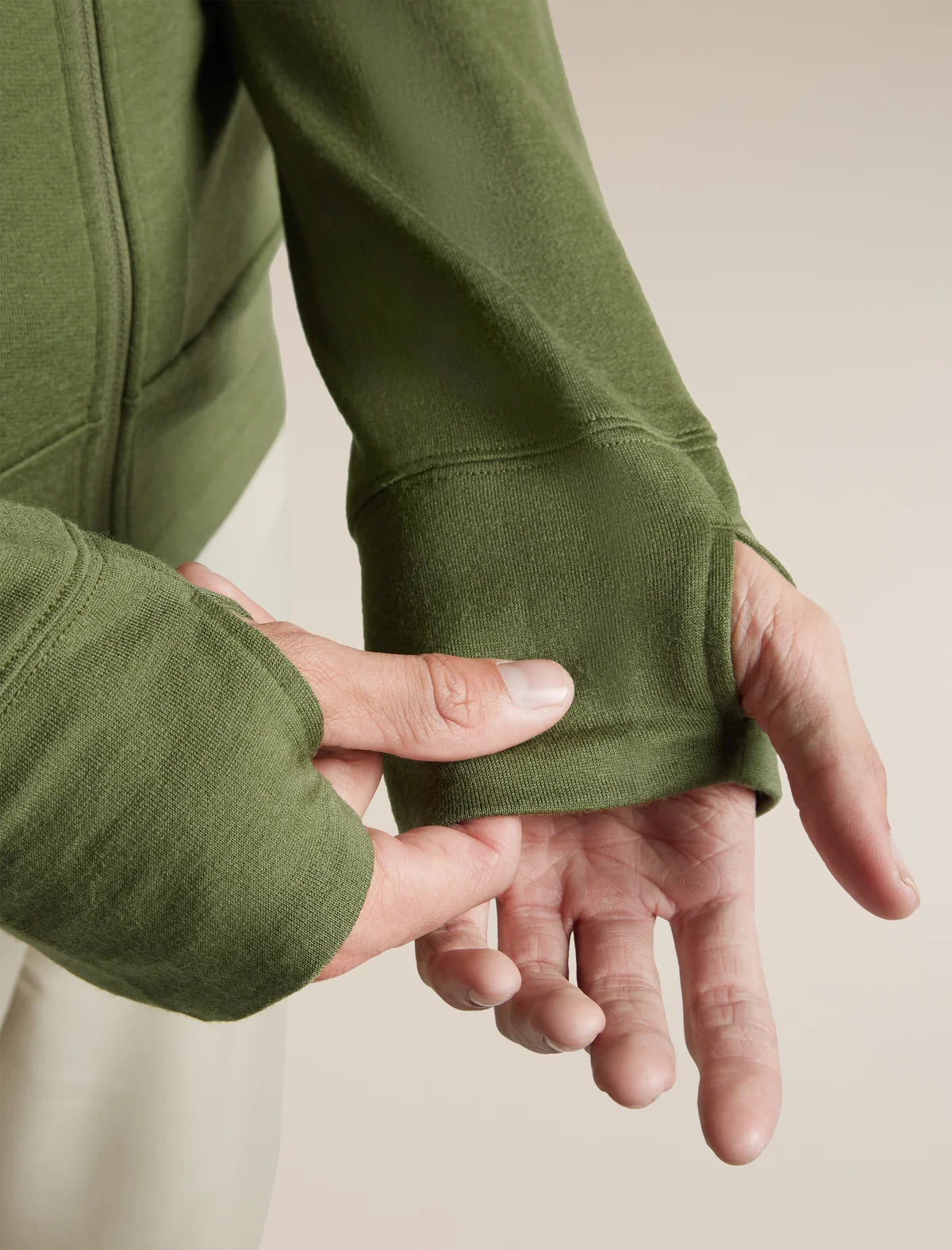 Close-up of a person's hands demonstrating the elasticized, cuffless sleeve construction of an olive green sweatshirt against a neutral beige background. - Icebreaker Merino 260 Quantum Long Sleeve Zip Hoodie (Men's) - Sphagnum