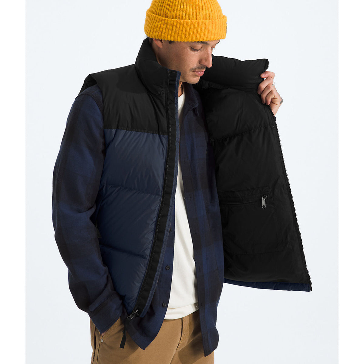 Person wearing a black and blue puffer jacket with a yellow beanie on a white background - The North Face 1996 Retro Nuptse Vest (Men's) - Summit Navy/TNF Black-Recycled Down