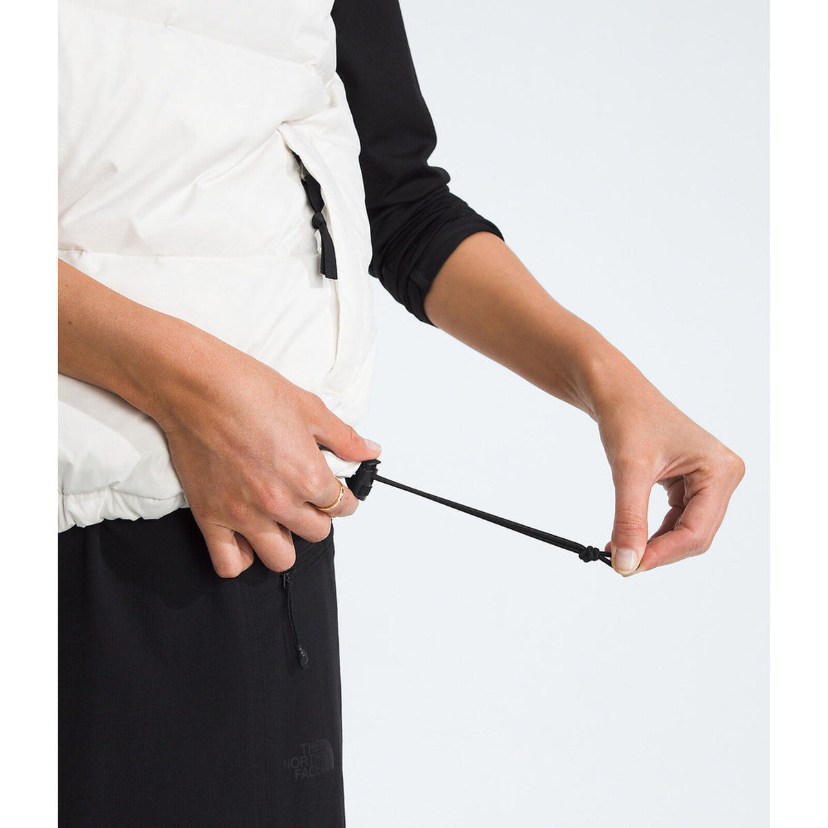 Person adjusting a drawstring on a bag against a white background - The North Face 1996 Retro Nuptse Vest (Womens) - White Dune/TNF Black-Recycled Down