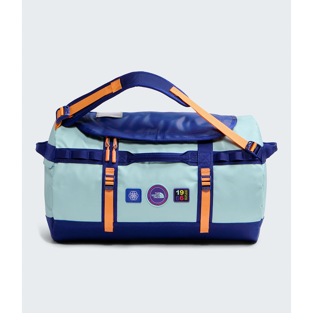 A light blue and navy duffel bag with bright orange straps and accents, featuring multiple brand patches on the front, set against a light gray background. - The North Face Base Camp Duffel Small 50L - Canal Blue/Bold Blue/Papaya