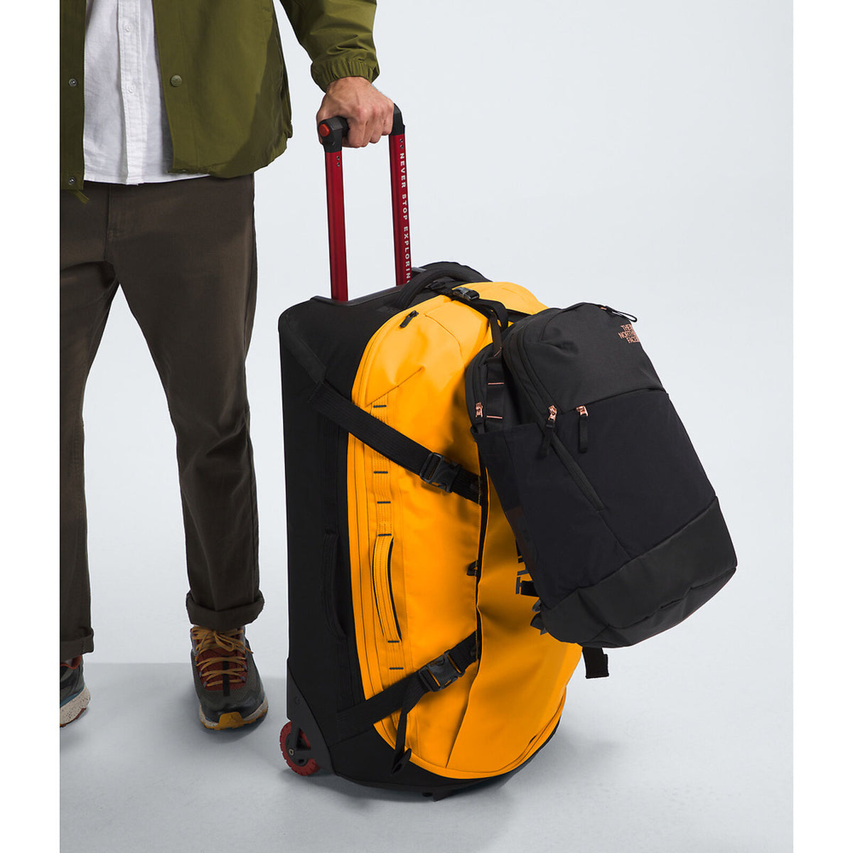 Person holding a yellow suitcase and black backpack against a light gray background - The North Face Base Camp Rolling Thunder 28" (95L) - Summit Gold/TNF Gold-NPF