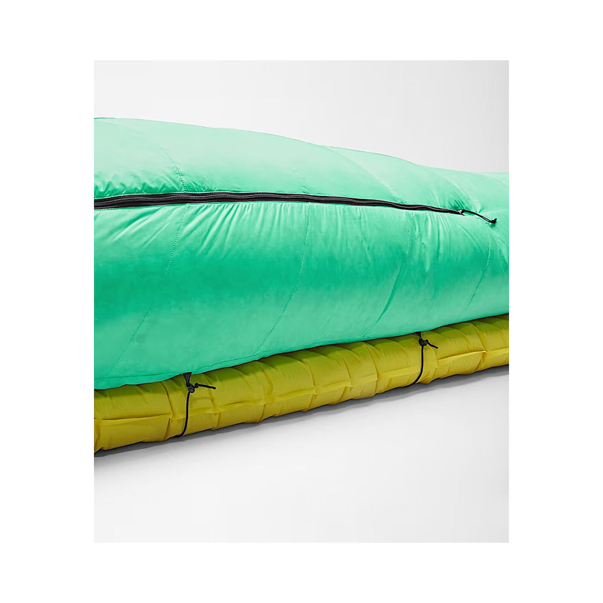 A close-up of a sleeping bag or camping mat with a bright mint green top section and a yellow lower section, separated by a black zipper, shown on a light gray studio background. - The North Face Inferno Sleeping Bag - 0F / -18C