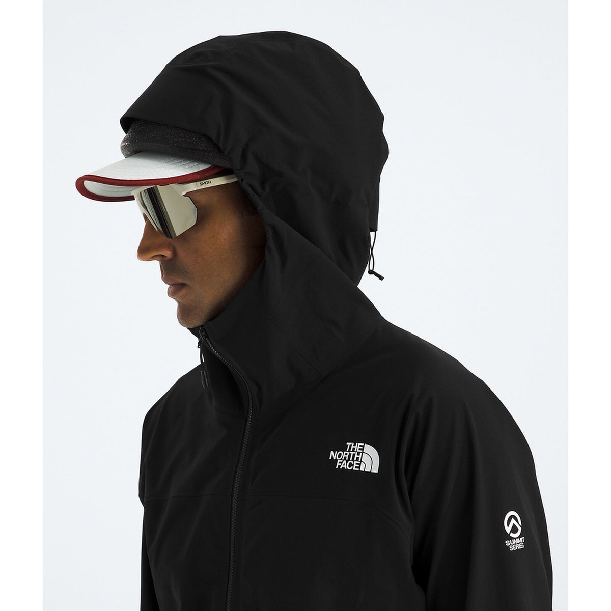 A man in profile wearing a black hooded jacket with a white embroidered The North Face logo on the chest, along with a visor and mirrored sunglasses, against a light gray background. - The North Face Summit Series Off Width Jacket (Men's) - TNF Black