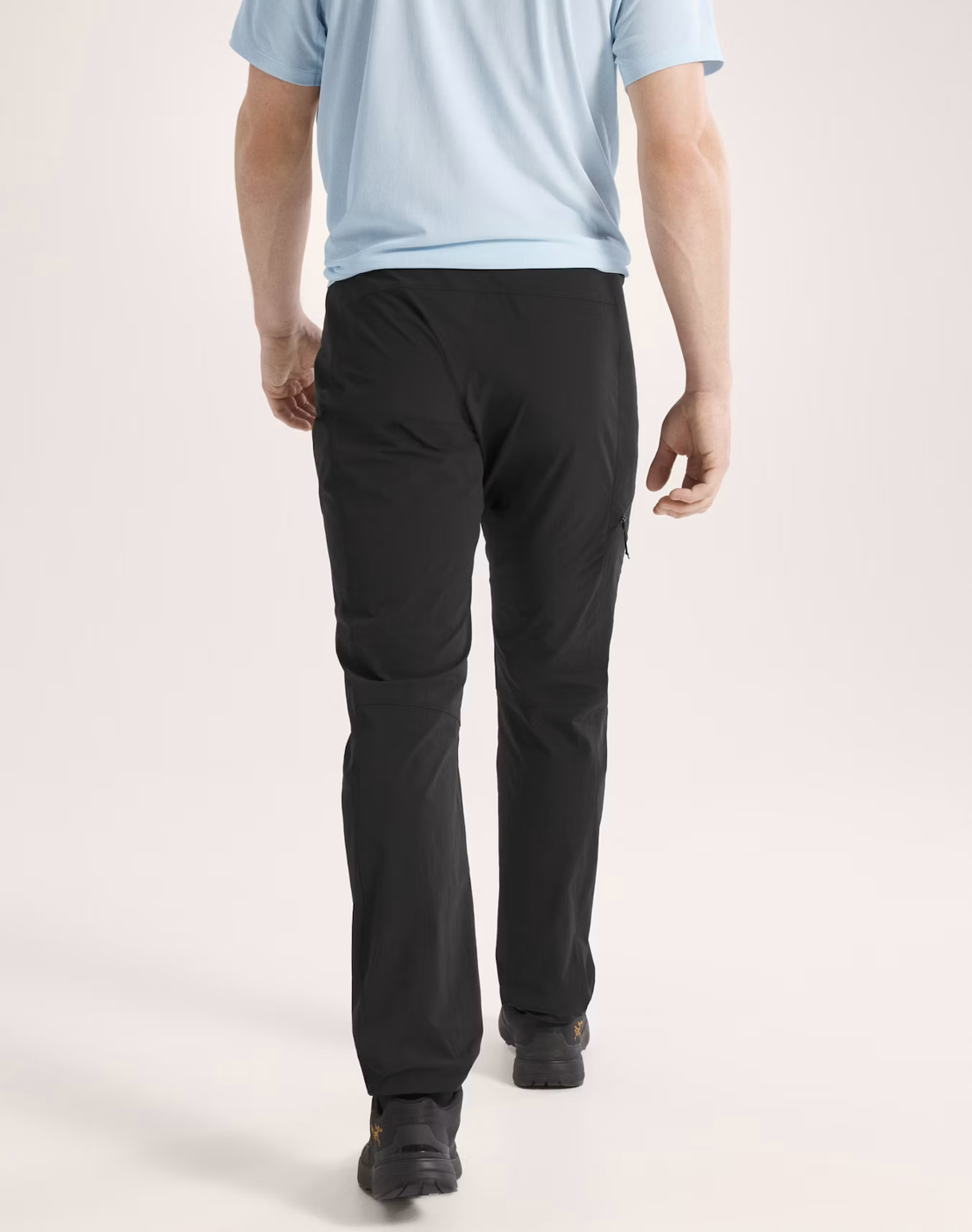 Rear view of a person wearing black pants and a light blue t-shirt, walking against a plain light beige studio background. - Arc'teryx Gamma SL Pants (Men's) - Black