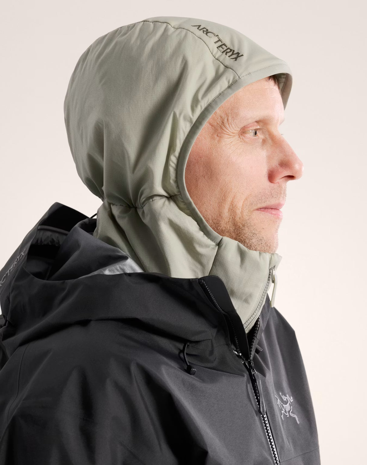 A man in profile wearing an Arc'teryx hooded jacket in a dark gray color, with the light gray hood up. The Arc'teryx logo is visible on the hood and chest. - Arc'teryx Atom Hoody (Men's) - Habitat