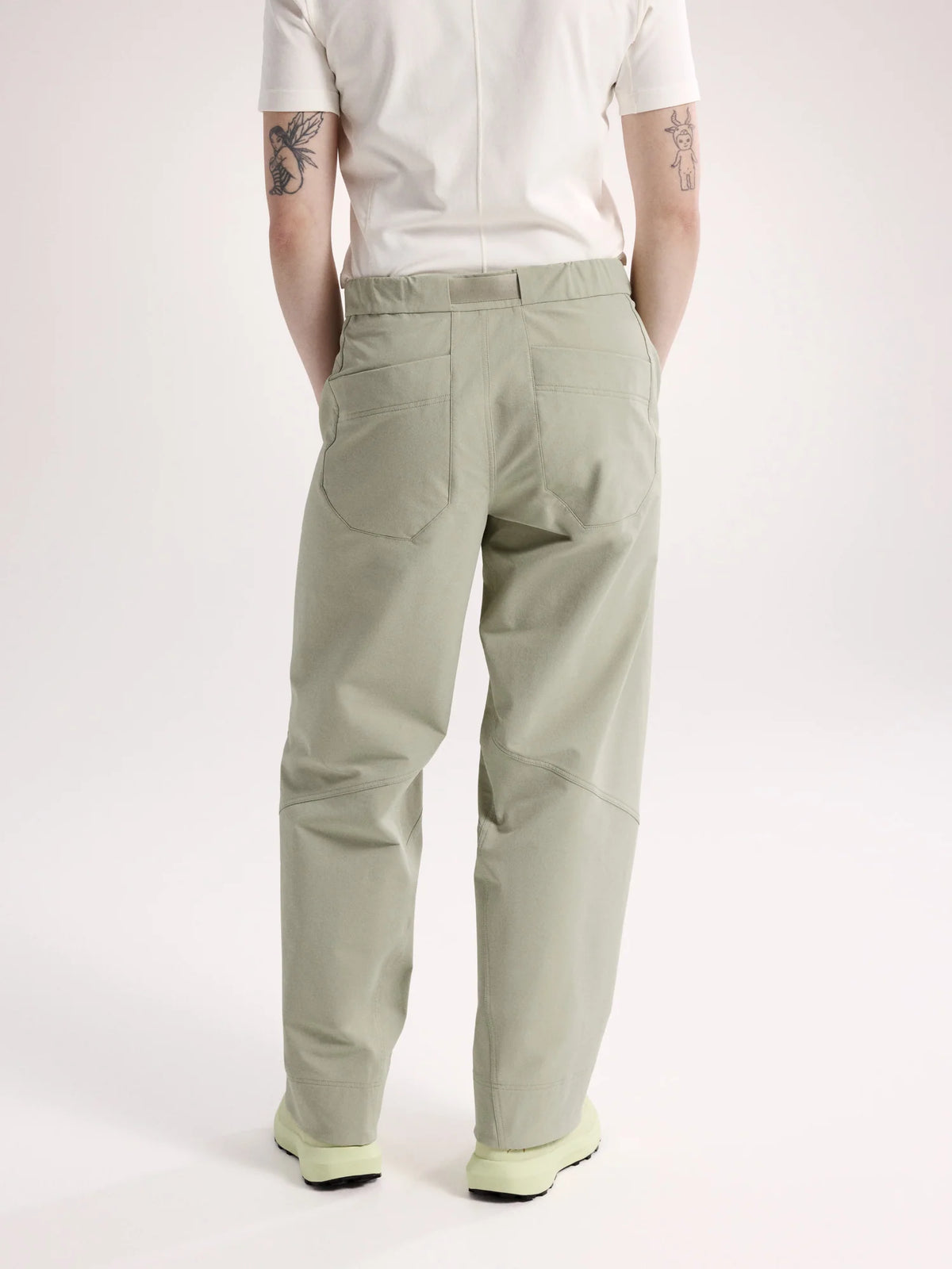 A person shown from the back wearing light sage green cargo pants, a white short-sleeve top, and light green sneakers against a plain light gray studio background. - Arc'teryx Nia Pants (Women's) - Habitat
