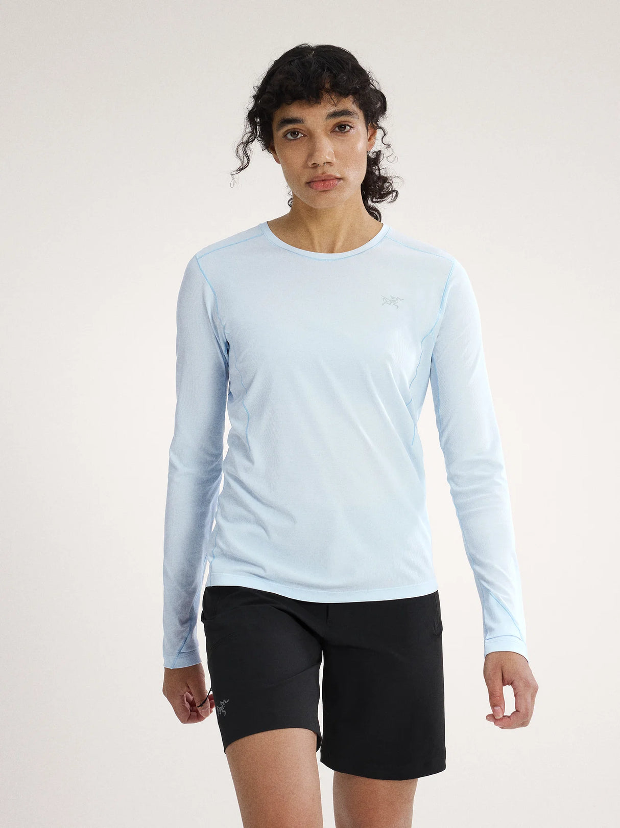 Person wearing a light blue long-sleeve shirt and black shorts on a white background - Arc'teryx Sunna Crew Shirt Long Sleeve (Women's) - Alpine Blue