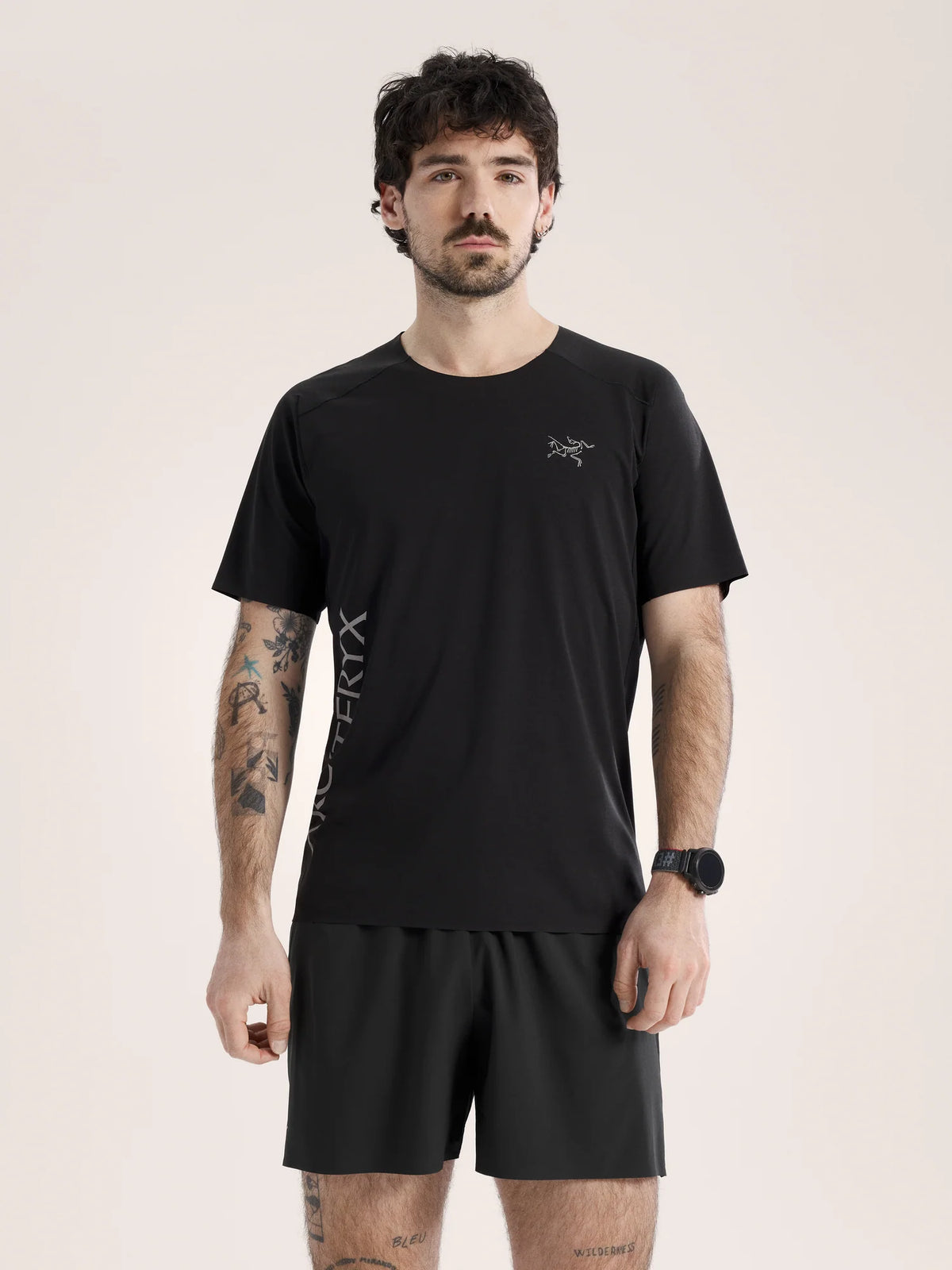 Man wearing a black t-shirt and shorts with a logo on a beige background - Arc'teryx Norvan Downword Logo Shirt Short Sleeve (Men's) - Black