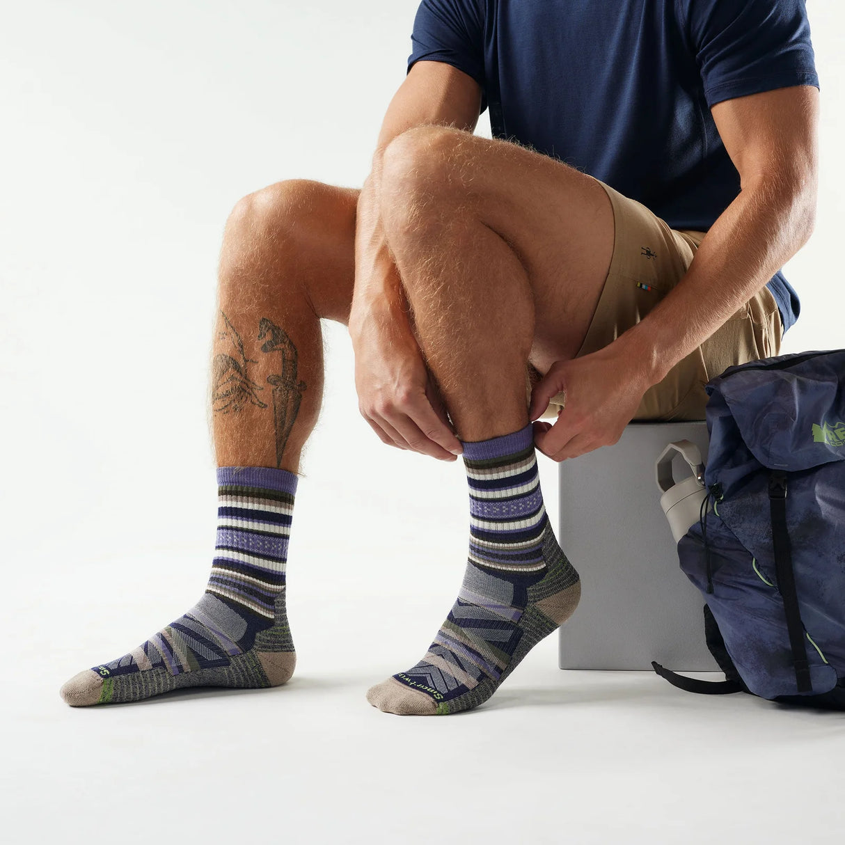 Person wearing striped socks sitting with a backpack on a white background - Smartwool Hike Panorama Light Cushion Crew Socks (Unisex) - Nightfall Blue