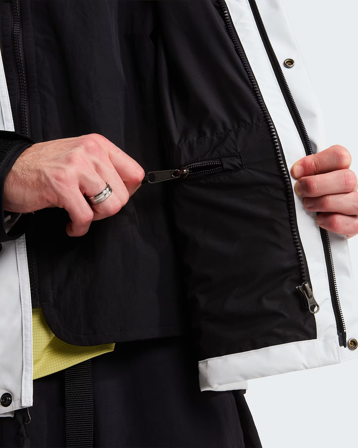 Close-up of a person wearing a black and white jacket, showing hands opening a zippered pocket on the black side panel. - The North Face GORE-TEX Mountain Jacket (Men's) - Pearl Stone/TNF Black