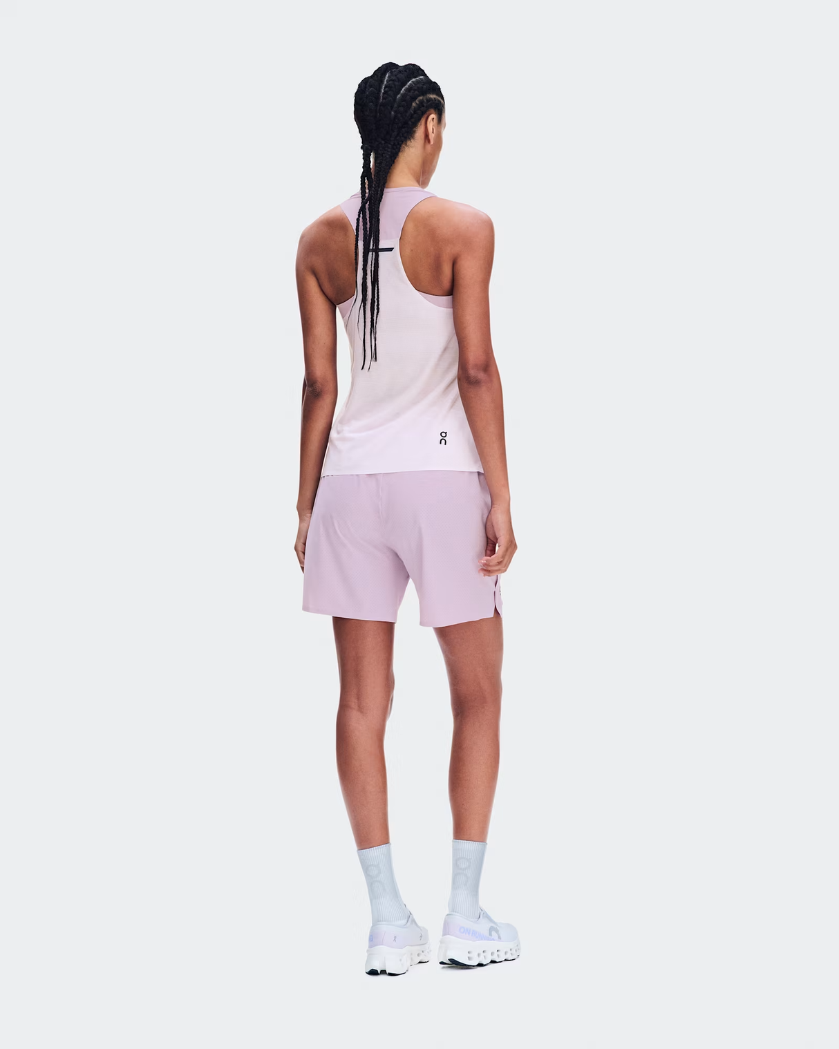 A model shown from the back wearing a light pink athletic tank top and matching light pink shorts, paired with white socks and white sneakers, against a solid light gray background. - On Performance Tank (Women's) - Foxglove/Orchid