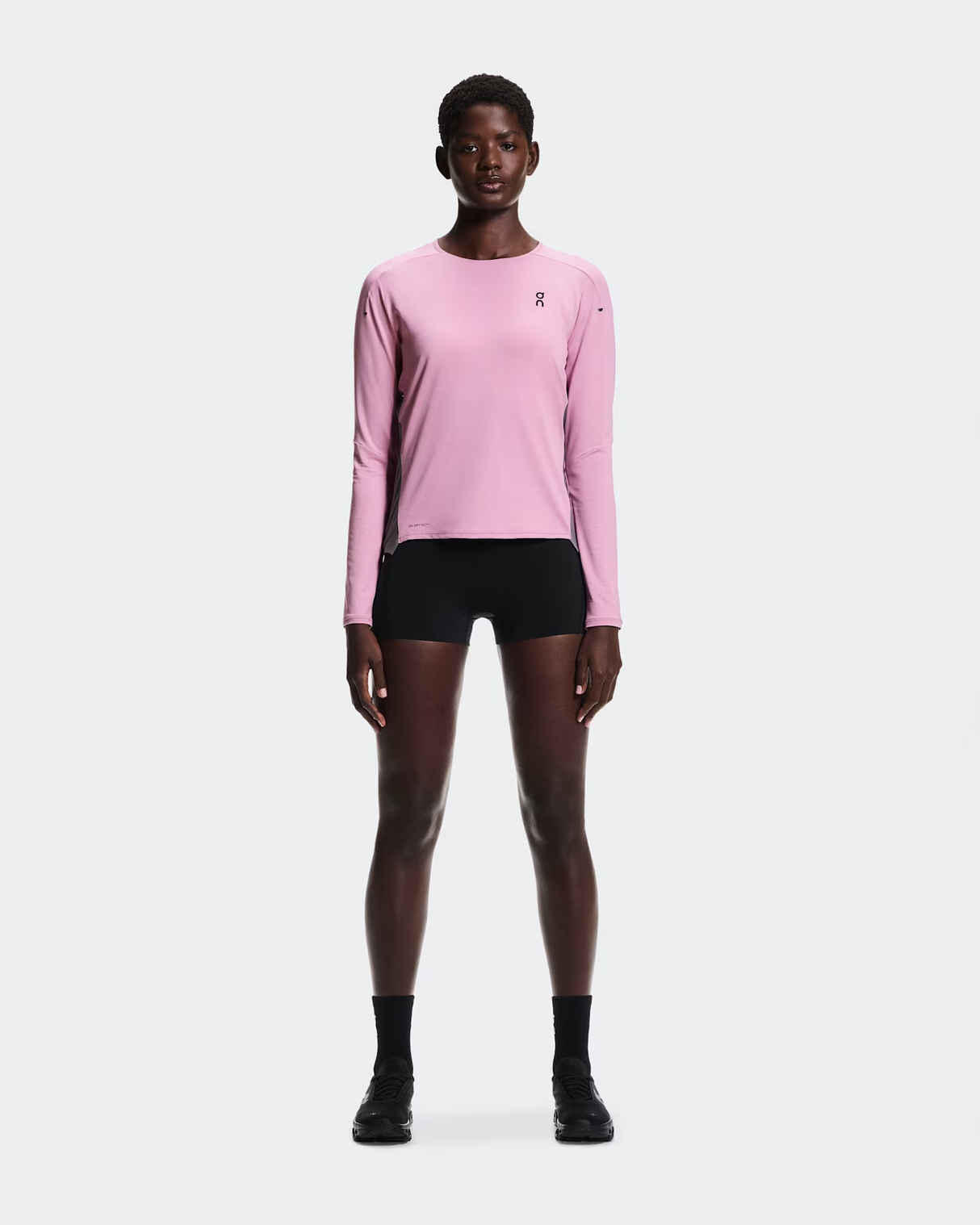 Person wearing a pink long-sleeve athletic shirt and black shorts on a white background - On Performance Long-T (Women's) - Dewberry/Sakura
