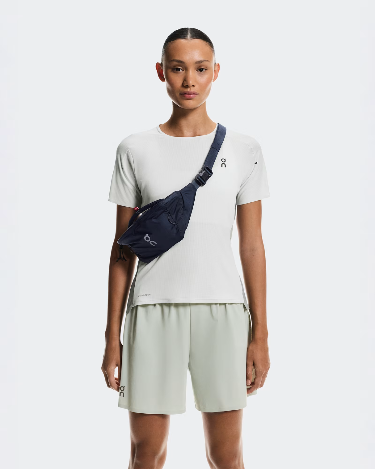 Person wearing a white t-shirt and light-colored shorts with a navy crossbody bag on a white background - On Waist Pack 2L Lite - Navy