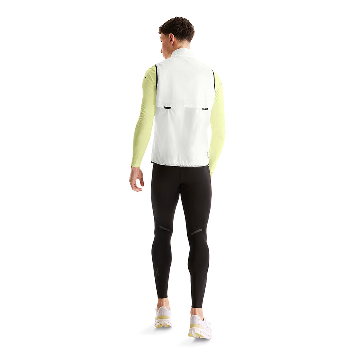 Person wearing a white vest, green long-sleeve shirt, black leggings, and white shoes on a white background - On Weather Vest (Men's) - White/Black