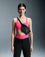 Woman wearing a pink sports bra and black leggings with a black crossbody bag on a gray background - On Waist Pack 2L Lite - Magnet