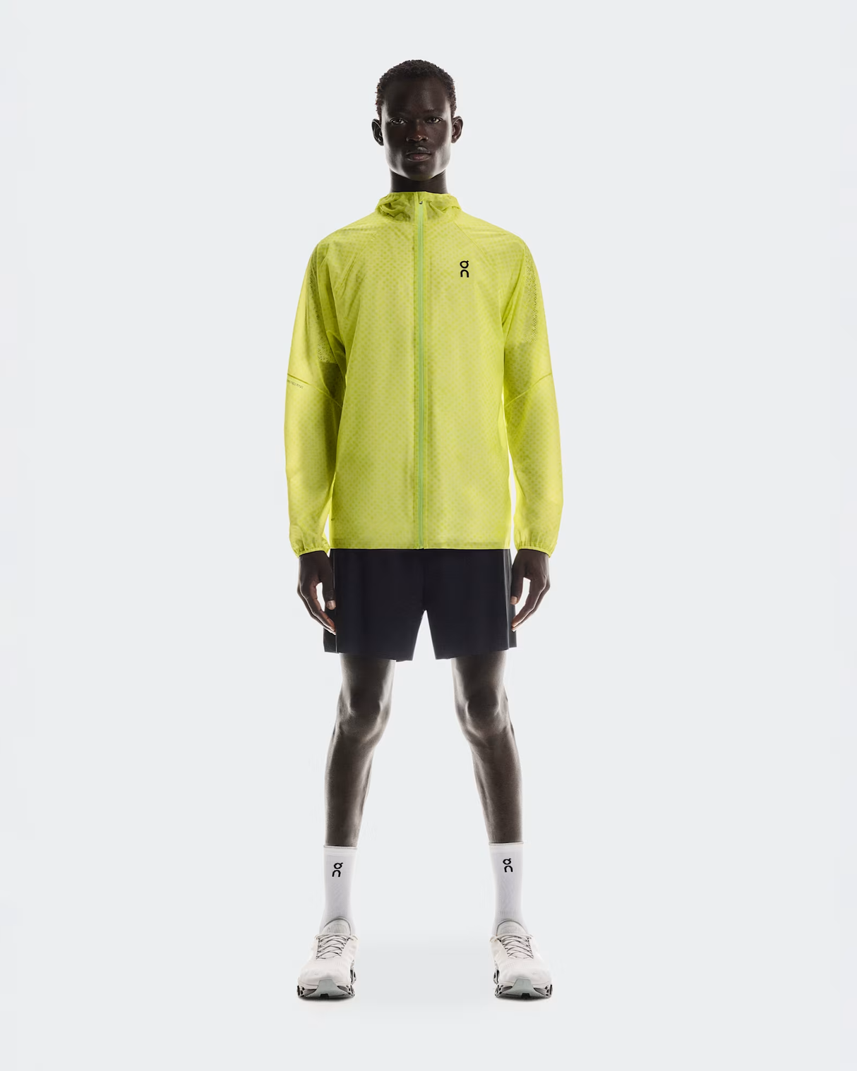 Person wearing a bright yellow running jacket and black shorts on a white background - On Ultra Jacket (Men's) - Limelight/Lime