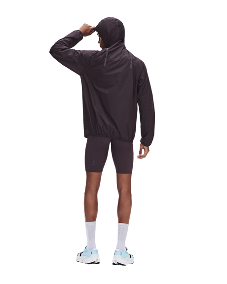A man wearing a dark brown hooded windbreaker jacket and matching biker shorts, shown from the back against a solid white background. - On Ultra Jacket (Men's) - Urchin