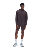 A male model wearing a dark brown athletic windbreaker jacket, matching shorts, white socks, and white sneakers with light blue accents, standing against a solid white background. - On Ultra Jacket (Men's) - Urchin