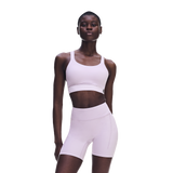 A model wearing a light pink matching activewear set consisting of a sports bra and high-waisted biker shorts, photographed against a solid white background. - On Performance Bra (Women's) - Foxglove
