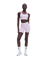 A model wearing a light pink athletic set consisting of a sports bra and matching high-waisted biker shorts, paired with white socks and white sneakers, set against a solid white background. - On Performance Bra (Women's) - Foxglove
