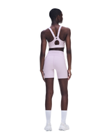 A model shown from the back wearing a light pink athletic set consisting of a sports bra with an open back and matching high-waisted shorts, paired with white socks and white sneakers on a solid white background. - On Performance Bra (Women's) - Foxglove